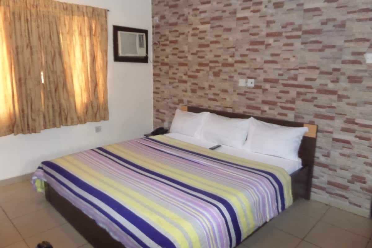 Un dormitorio con colcha a rayas, pared con diseño de ladrillo y ventana con cortinas.