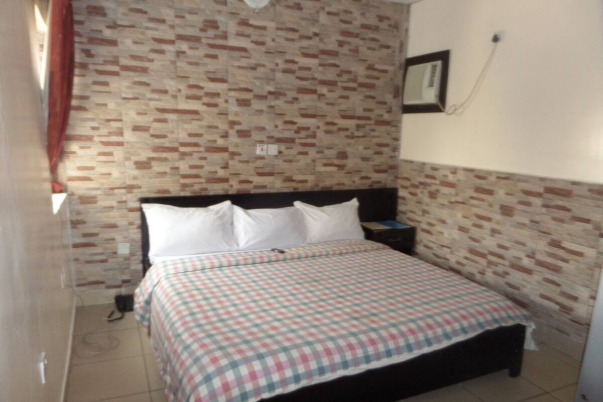 Un dormitorio con edredón a cuadros, pared con estampado de ladrillo, mesita de noche y espejo.