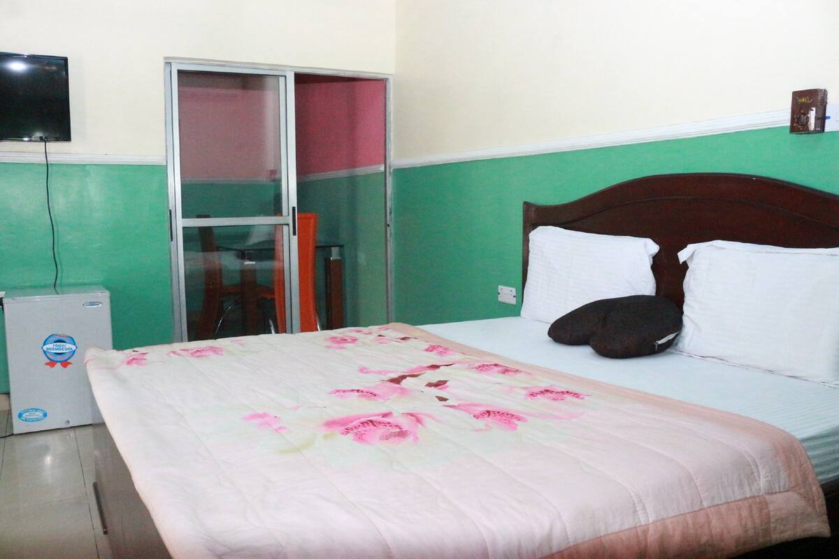 A bedroom with a bed, a television mounted on the wall, and a small refrigerator.