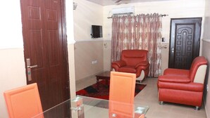 A living room with a glass table, two red chairs, a red sofa, a brown door, and a curtain. - L & L Executive Hotels and Suites (Uyo)