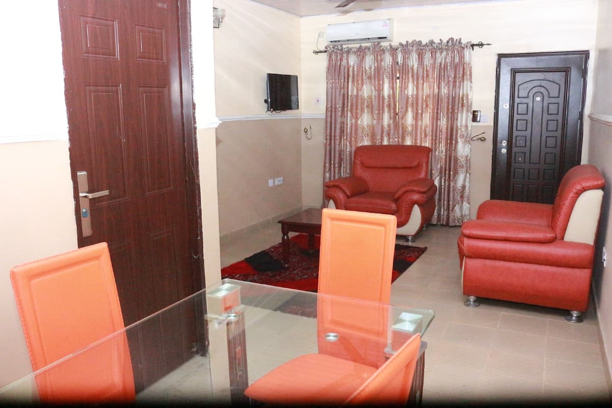 A living room with a glass table, two red chairs, a red sofa, a brown door, and a curtain.