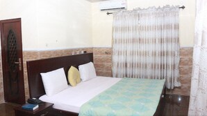 A hotel room with a bed, a nightstand, a telephone, and an air conditioning unit. - L & L Executive Hotels and Suites (Uyo)