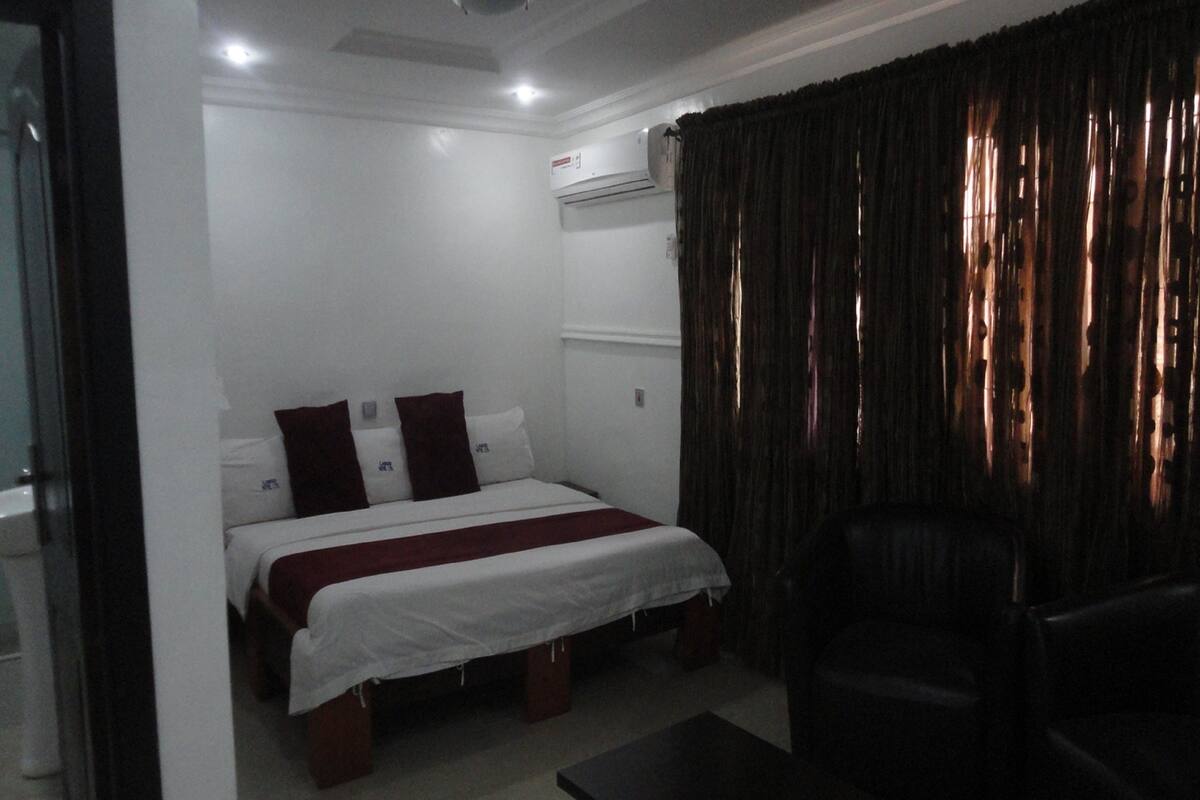 A hotel room with a bed, a chair, a table, and a window with curtains.