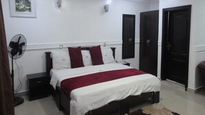 A bedroom with a bed, bedside tables, a fan, and a door. - Labod Hotel (Ibadan)