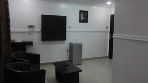 A room with a flat-screen TV mounted on the wall, a small table, and a trash bin. - Labod Hotel (Ibadan)