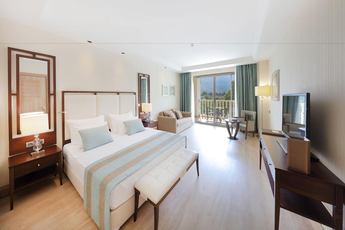 A hotel room with a large bed, a sofa, a TV, and a balcony with a view.