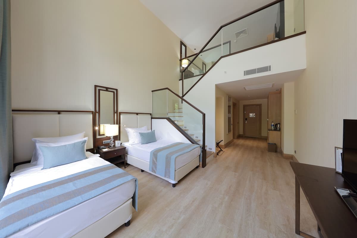 A hotel room with two beds, a staircase, a TV, and a small kitchenette.