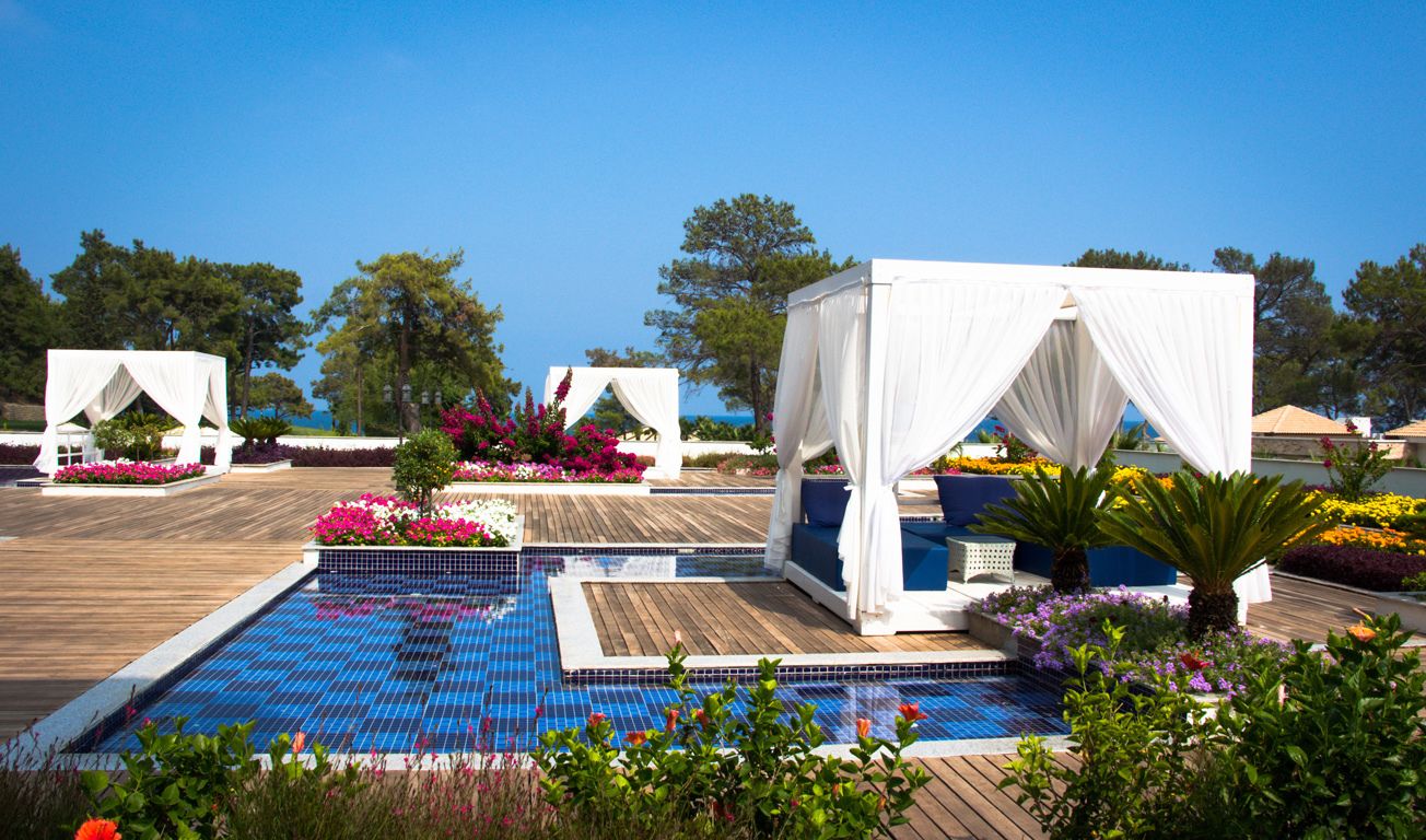 A pool area with a wooden deck, white canopies, and colorful flowers.