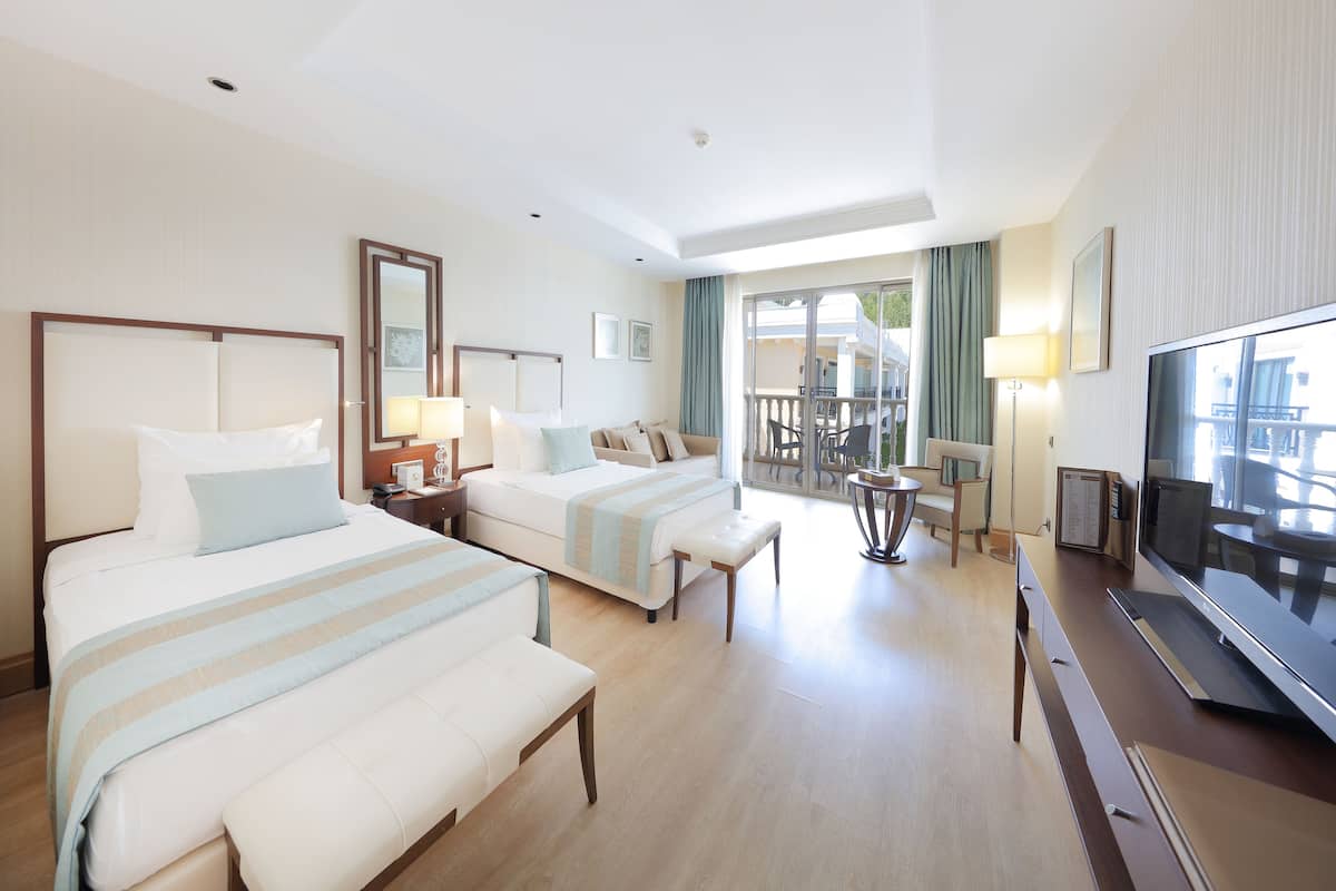 A hotel room with two beds, a TV, a desk, and a balcony with a view.