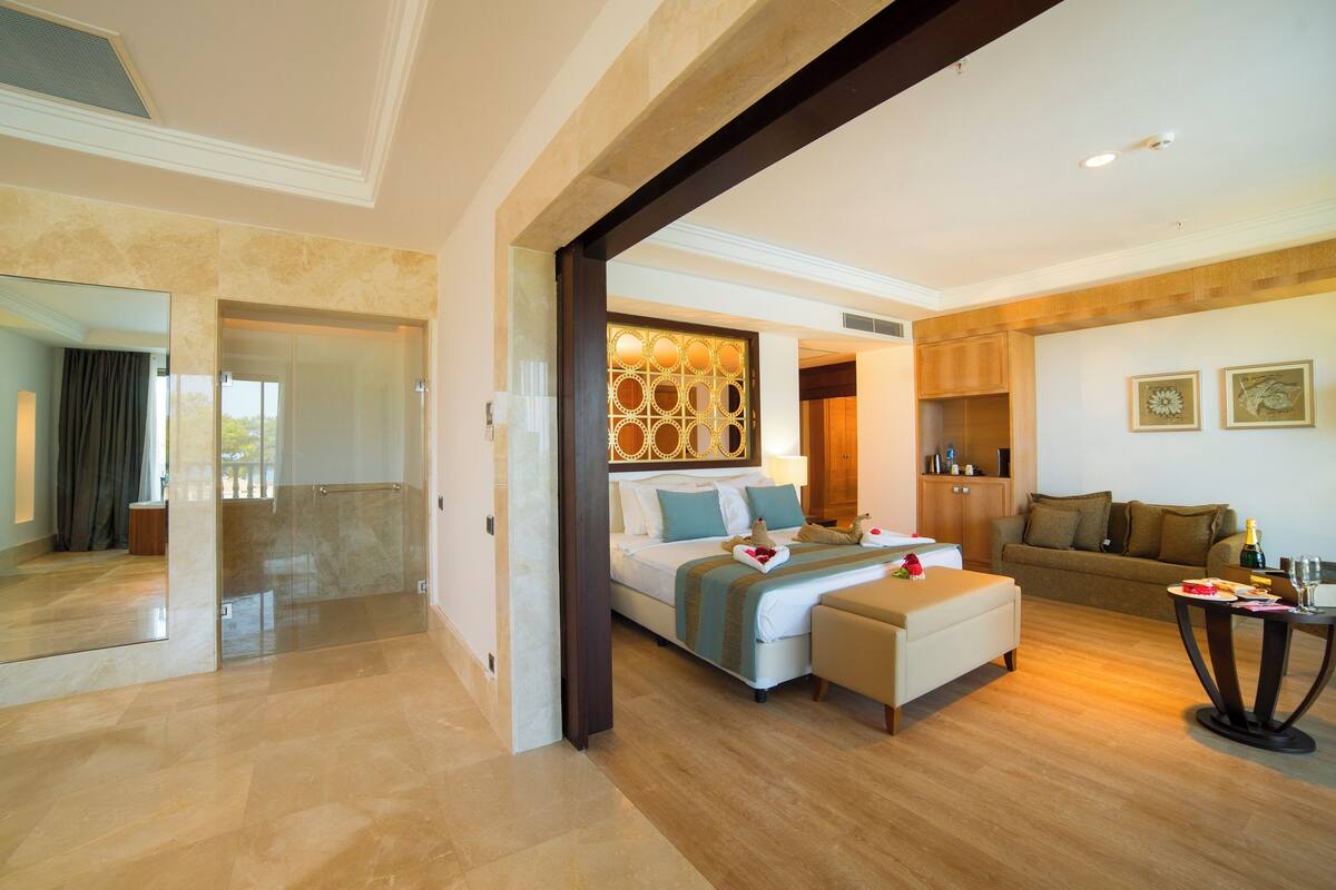 A spacious hotel room with a large bed, a sitting area, and a dining table.