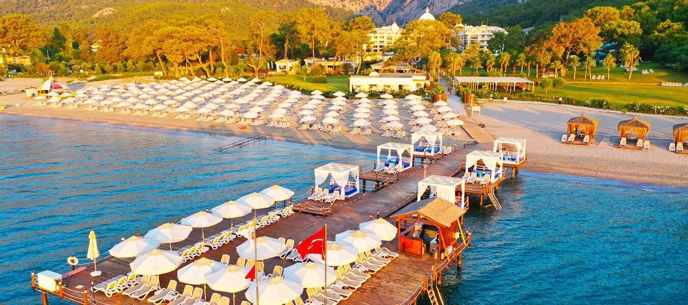 Ein Hotel am Wasser mit einer Anlegestelle, Liegestühlen, Sonnenschirmen und einem Poolbereich.