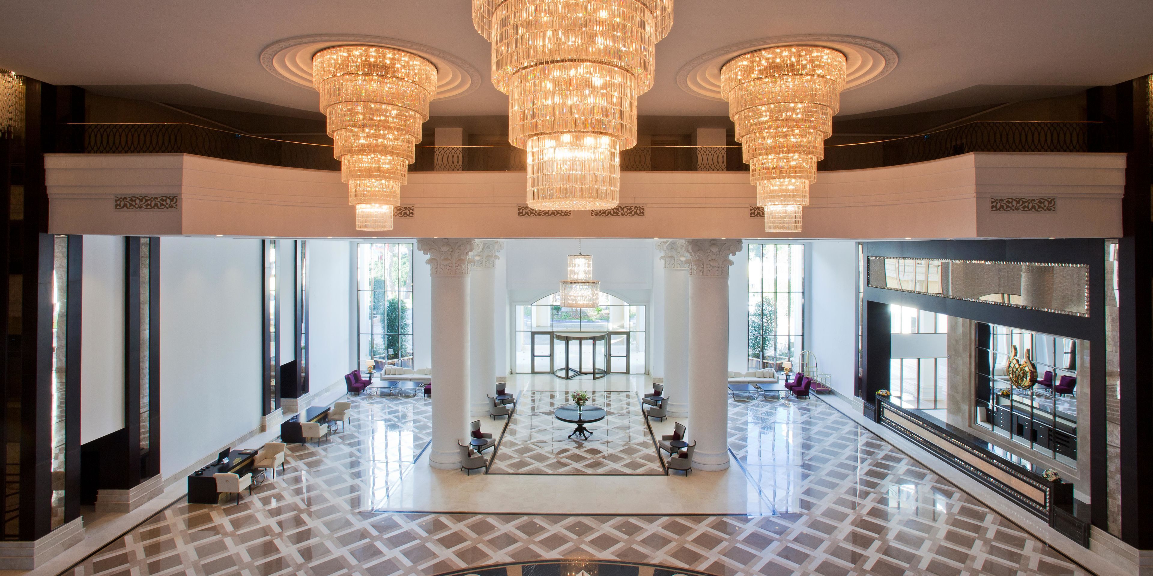 A spacious lobby with a grand chandelier, large windows, and a central seating area.