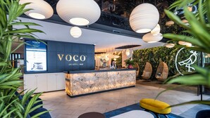 Un espace d’accueil doté d’un comptoir en marbre, d’un canapé bleu, d’un pouf jaune et de luminaires suspendus.