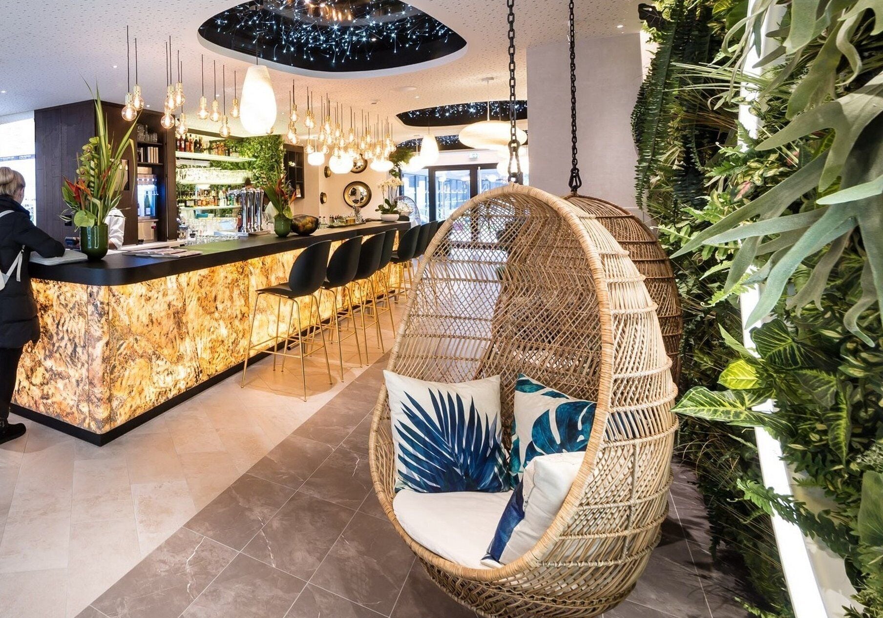 A modern interior with a bar area, hanging chairs, and indoor plants.