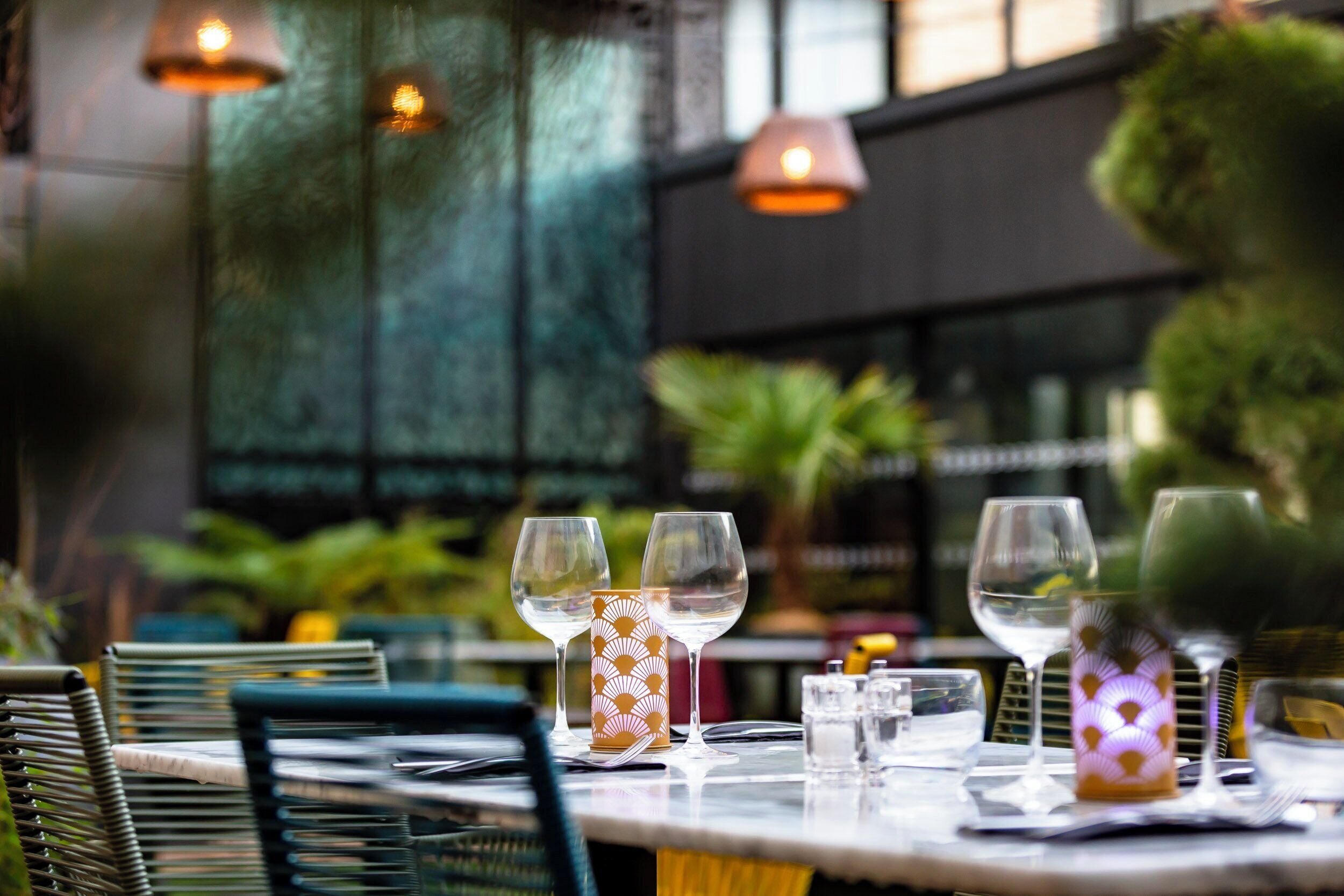 Una mesa dispuesta con copas de vino y un posavasos con diseño, con vistas a follaje y un edificio al fondo.