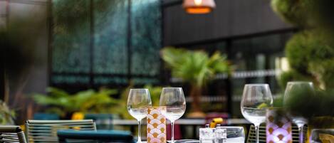 Una mesa dispuesta con copas de vino y un posavasos con diseño, con vistas a follaje y un edificio al fondo.