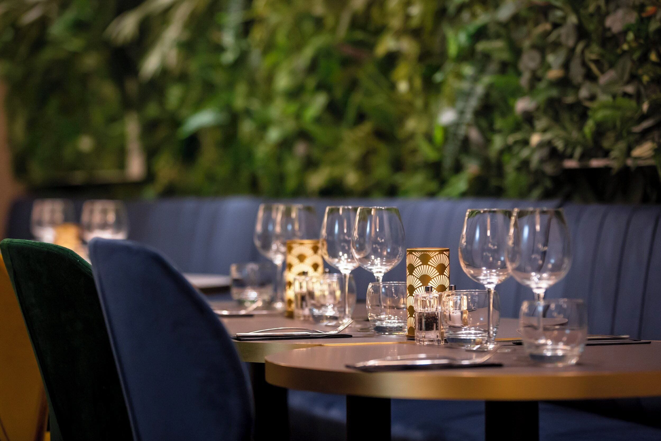 Un área de comedor con una fila de mesas, cada una con copas de vino, cubiertos y un candelabro.