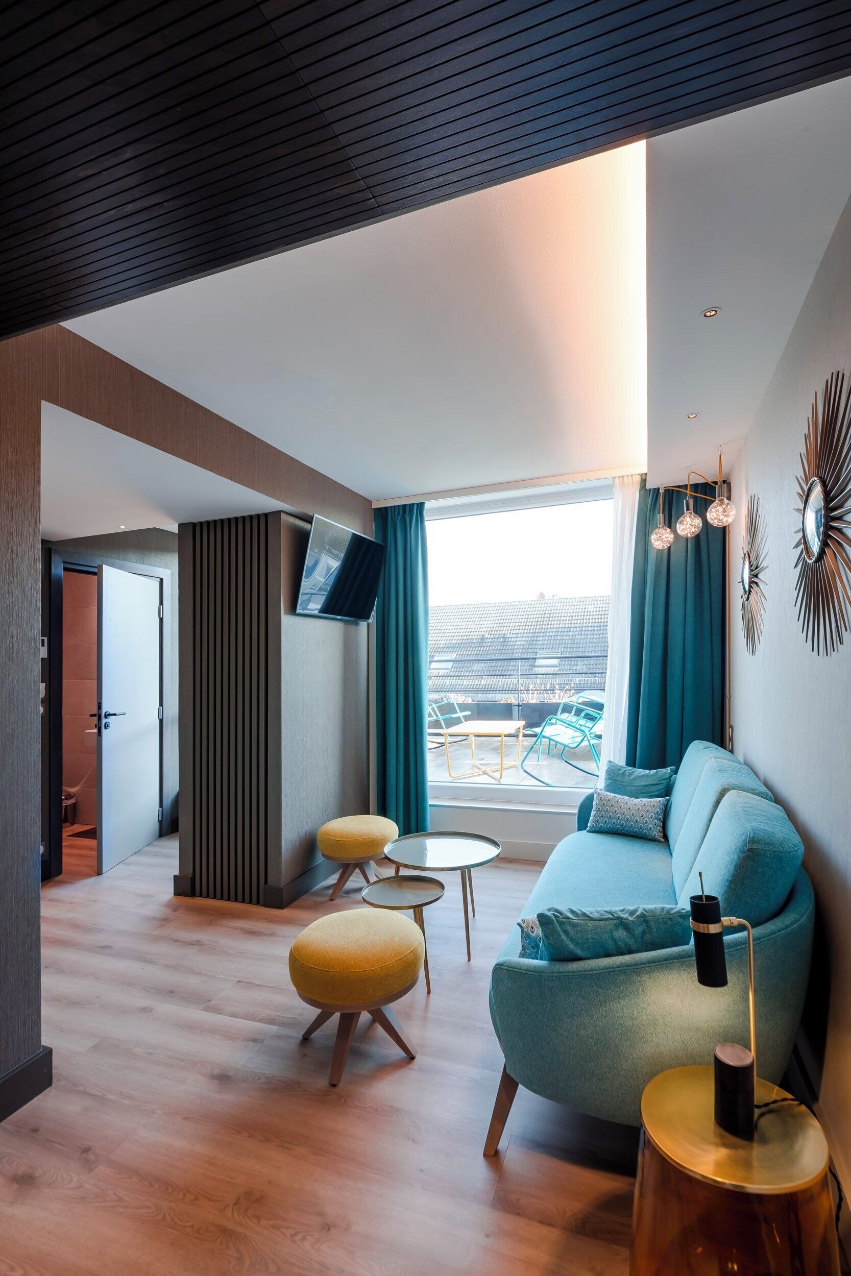 A modern living room with a sofa, ottomans, a TV, and a view of an outdoor seating area.