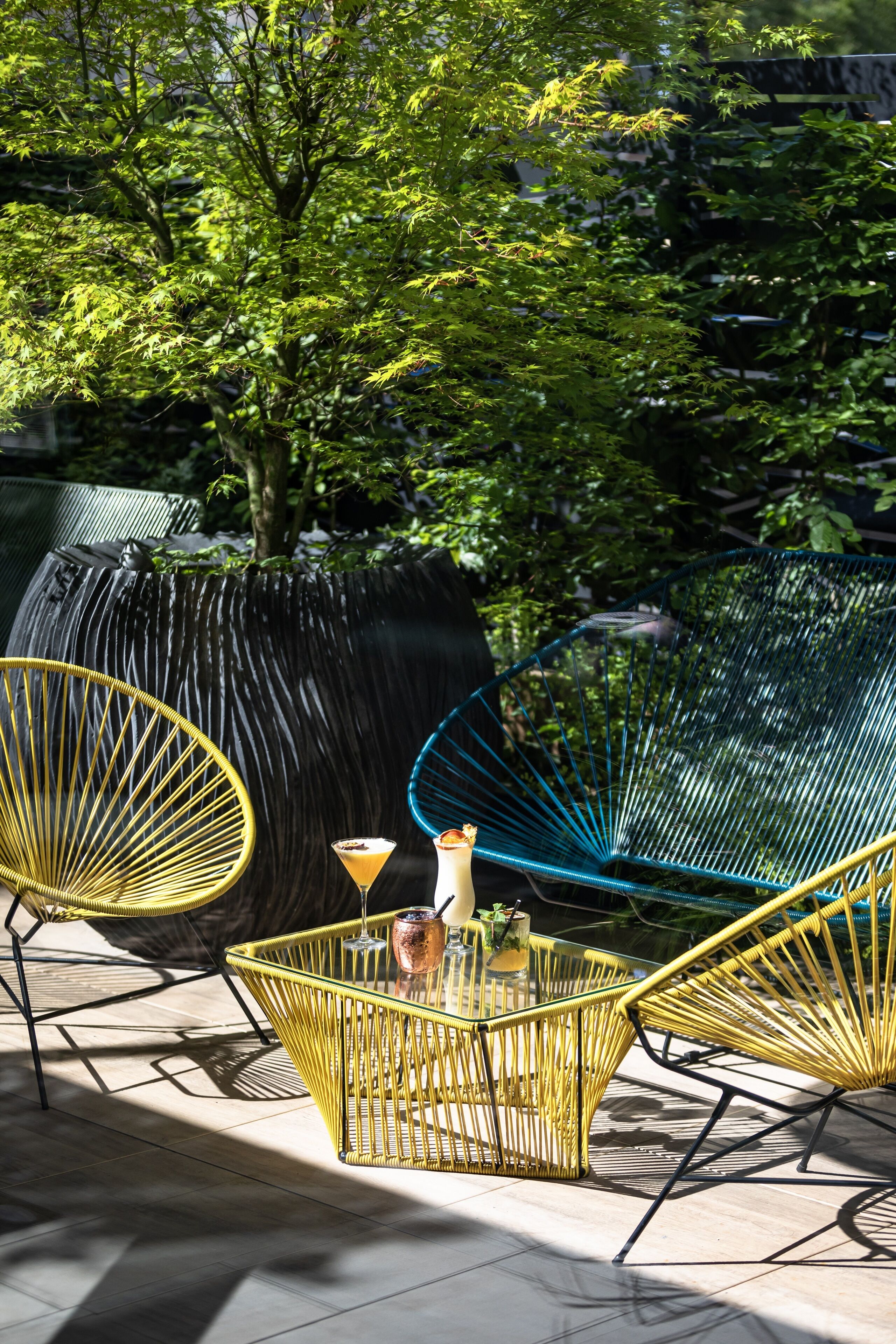 Een terras met geel- en blauwe rieten stoelen, een glazen tafel en een martini-glas.
