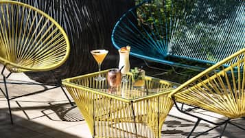 Een terras met geel- en blauwe rieten stoelen, een glazen tafel en een martini-glas.