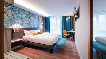 A hotel room with a bed, bedside table, bench, and a desk with a chair.