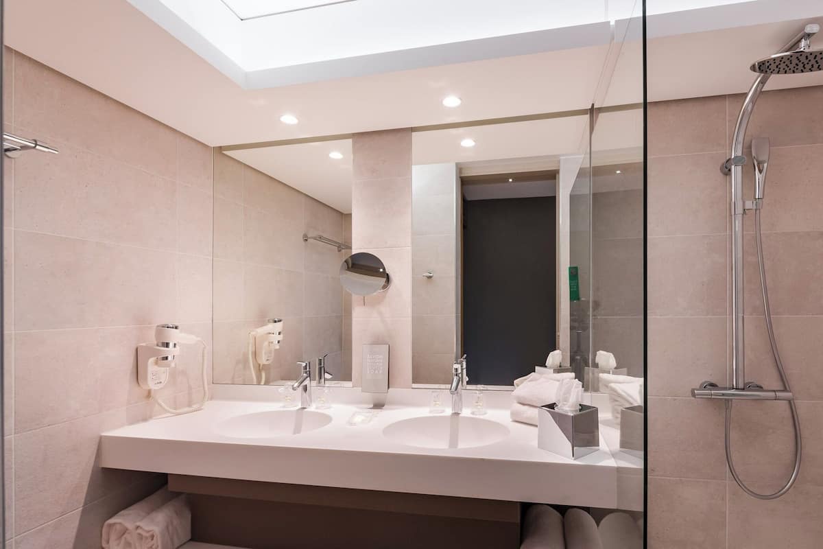 A modern bathroom with two sinks, a large mirror, a shower, and a skylight.