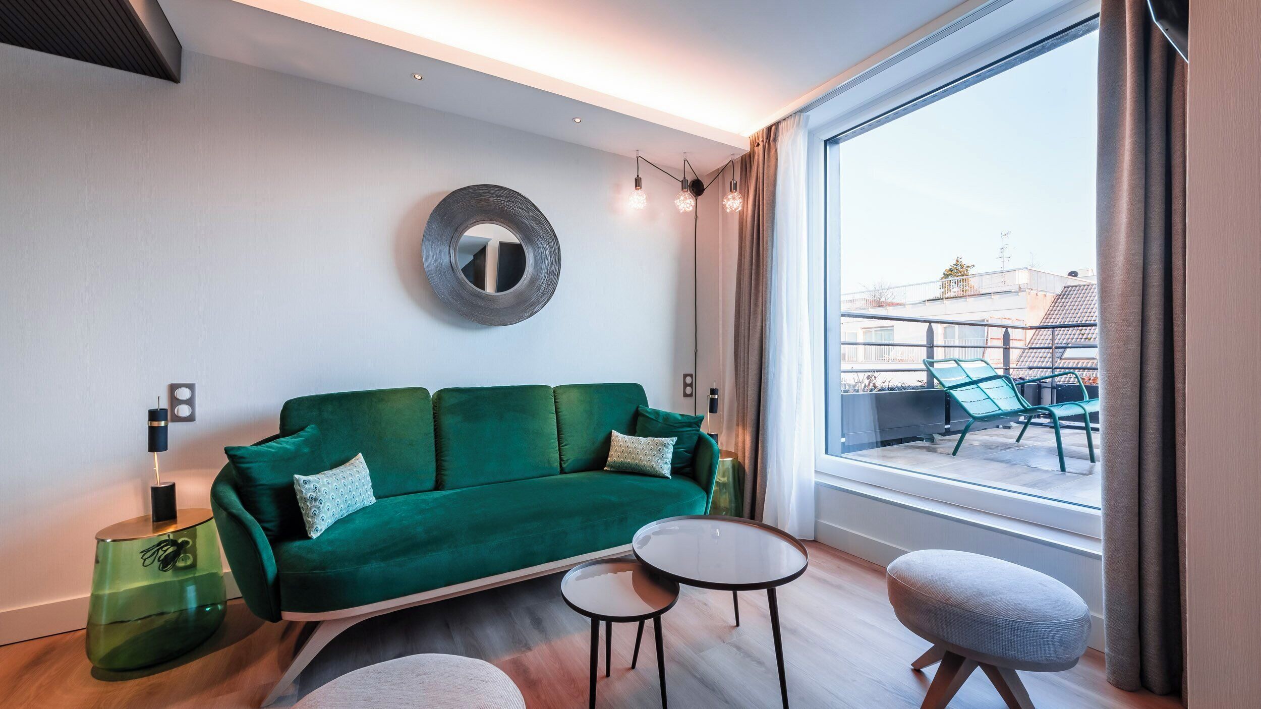 A modern living room with a green sofa, two small tables, and a large window with a view of buildings.