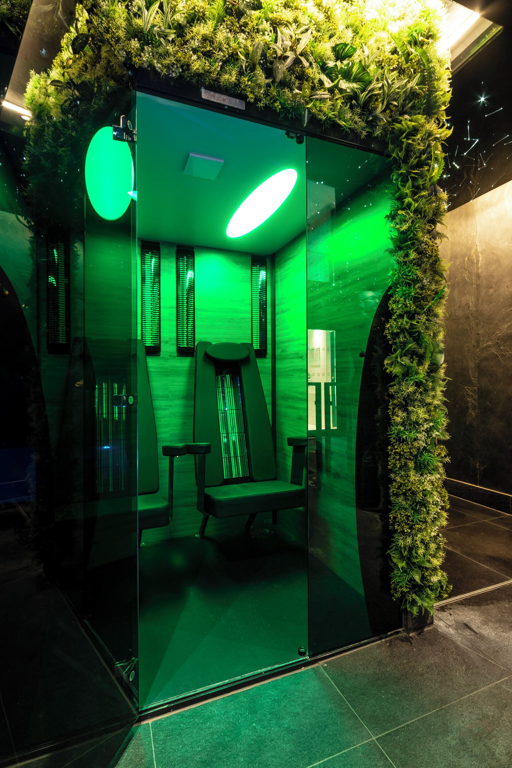 Een kamer met een glazen scheidingswand, sfeervol groen licht, een bank en een kleine tafel.