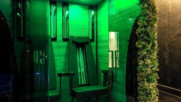 Een kamer met een glazen scheidingswand, sfeervol groen licht, een bank en een kleine tafel.
