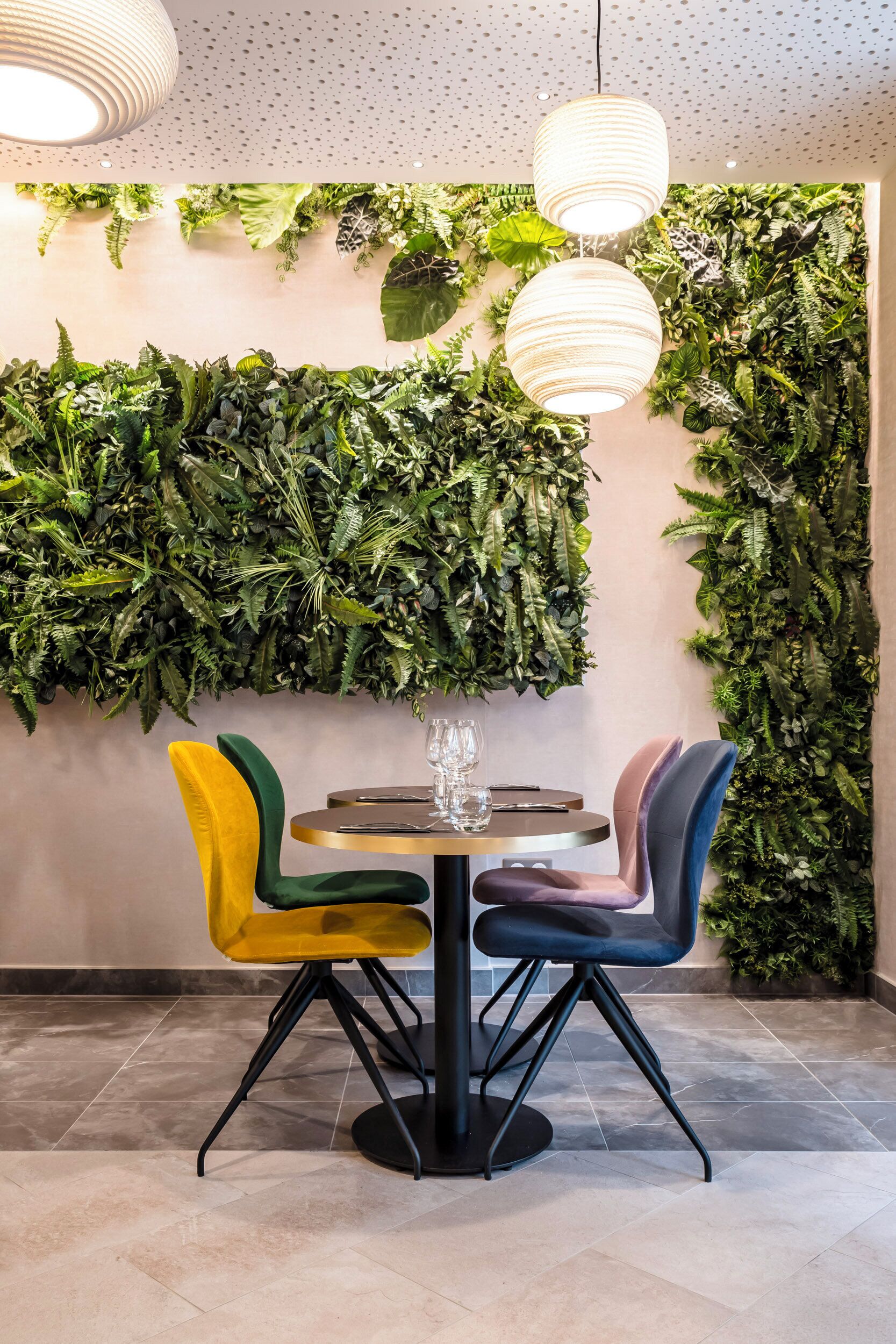 A dining area with a round table, colorful chairs, and a wall covered with green plants.