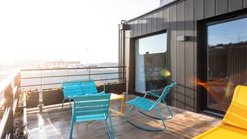 A rooftop terrace with two blue rocking chairs and a yellow sofa, overlooking a cityscape.