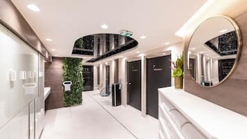 A modern hotel corridor with a glass wall, a green wall with plants, a mirror, and a reception desk.