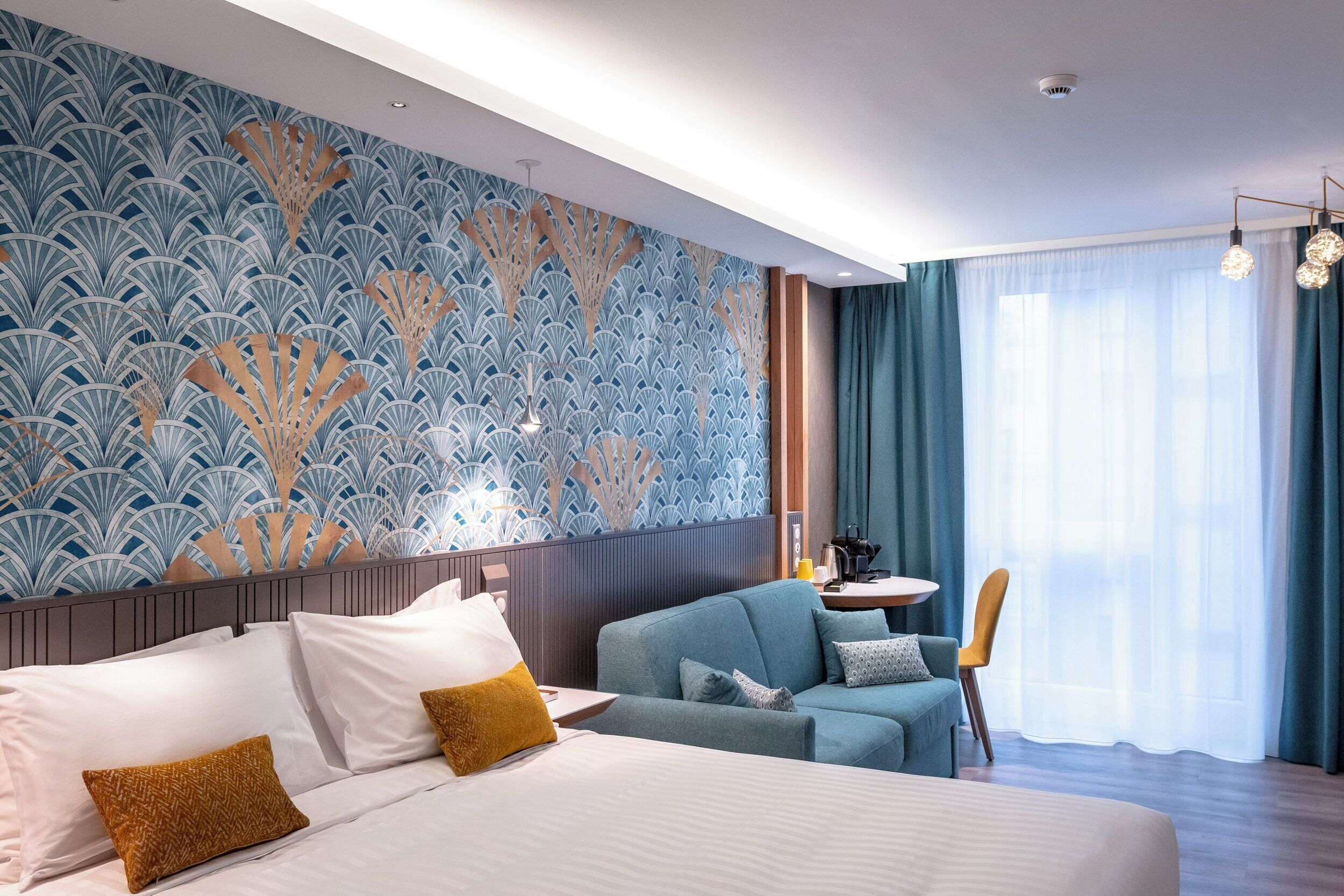 Une chambre d’hôtel avec un grand lit, un coin salon, un mur décoratif et une fenêtre avec des rideaux.