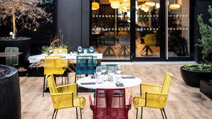 Un espace de restauration en plein air avec des chaises jaunes et rouges, une table ronde et des lampes suspendues.