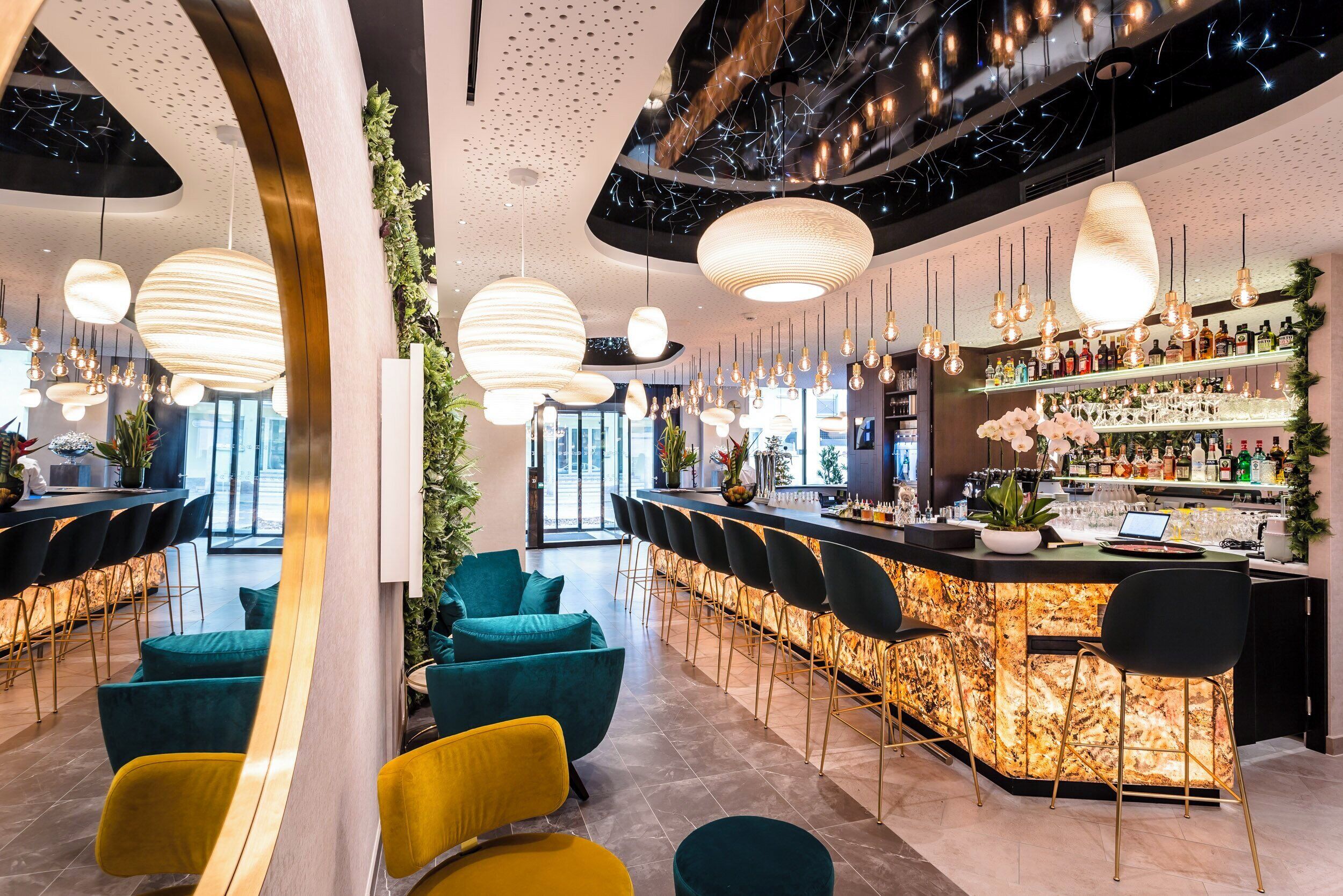 Zona de bar con barra curva, varias lámparas colgantes y diversas opciones de asientos, incluyendo taburetes y sillas acolchadas.