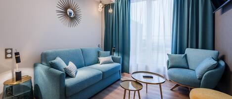 Una sala de estar moderna con un sofá azul, un sillón a juego, una pequeña mesa redonda y un espejo decorativo en la pared.