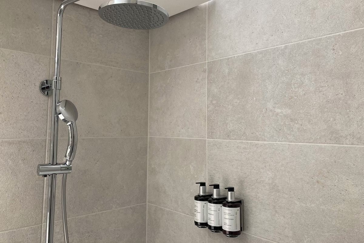 A modern shower with a rain shower head and handheld showerhead, mounted on a wall with grey tiles.