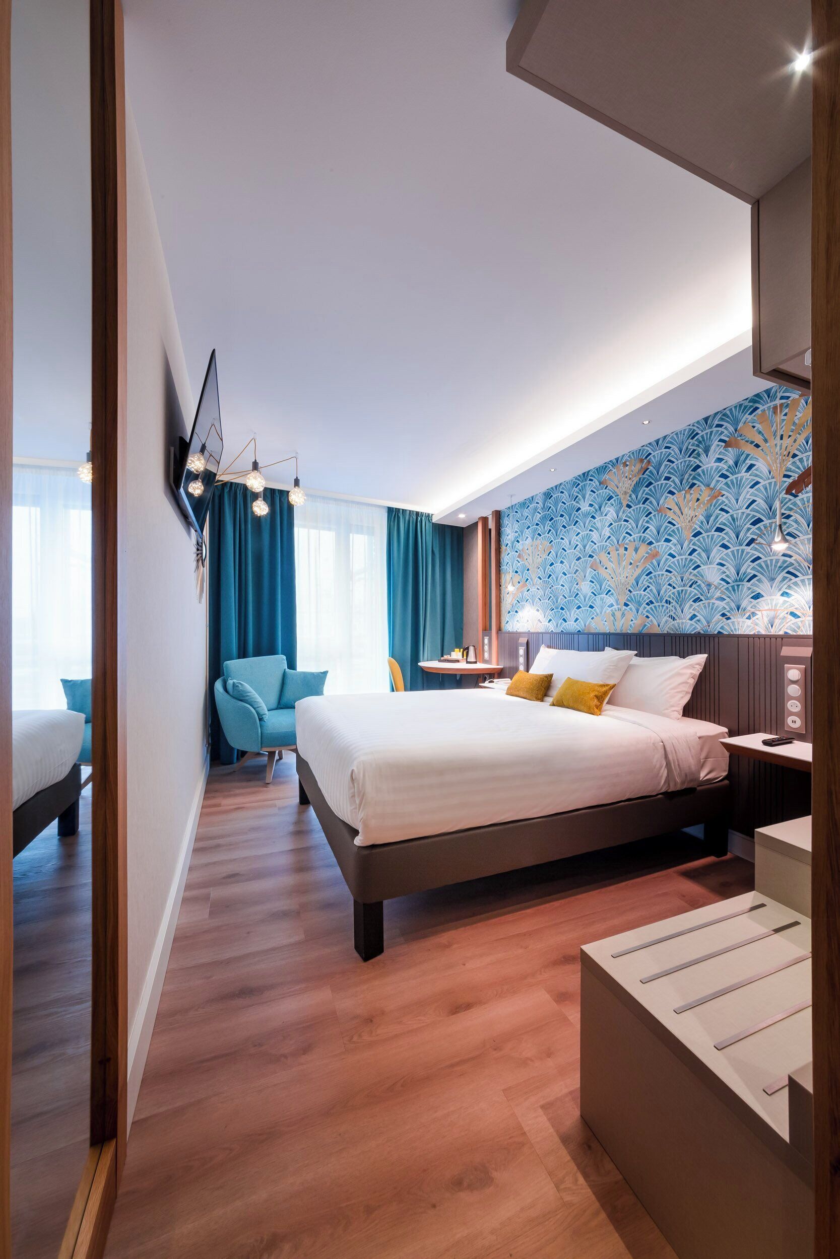 A modern hotel room with a large bed, a seating area with a blue chair, and a decorative wall.