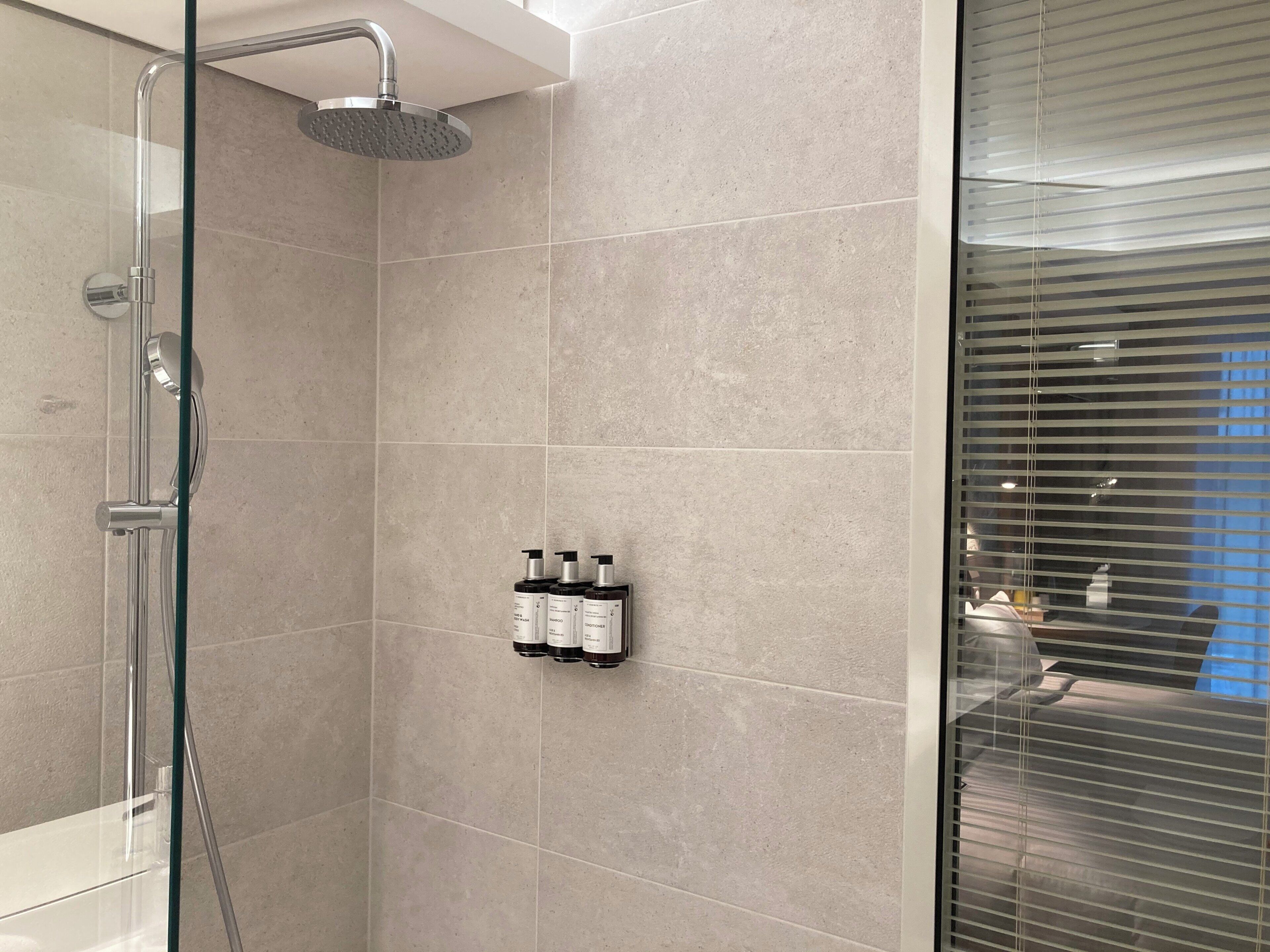 A modern bathroom with a glass-enclosed shower, beige tiles, and a wall-mounted bottle rack.
