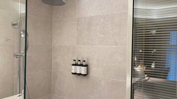 Un baño moderno con ducha de vidrio, azulejos color beige y un perchero para botellas en la pared.