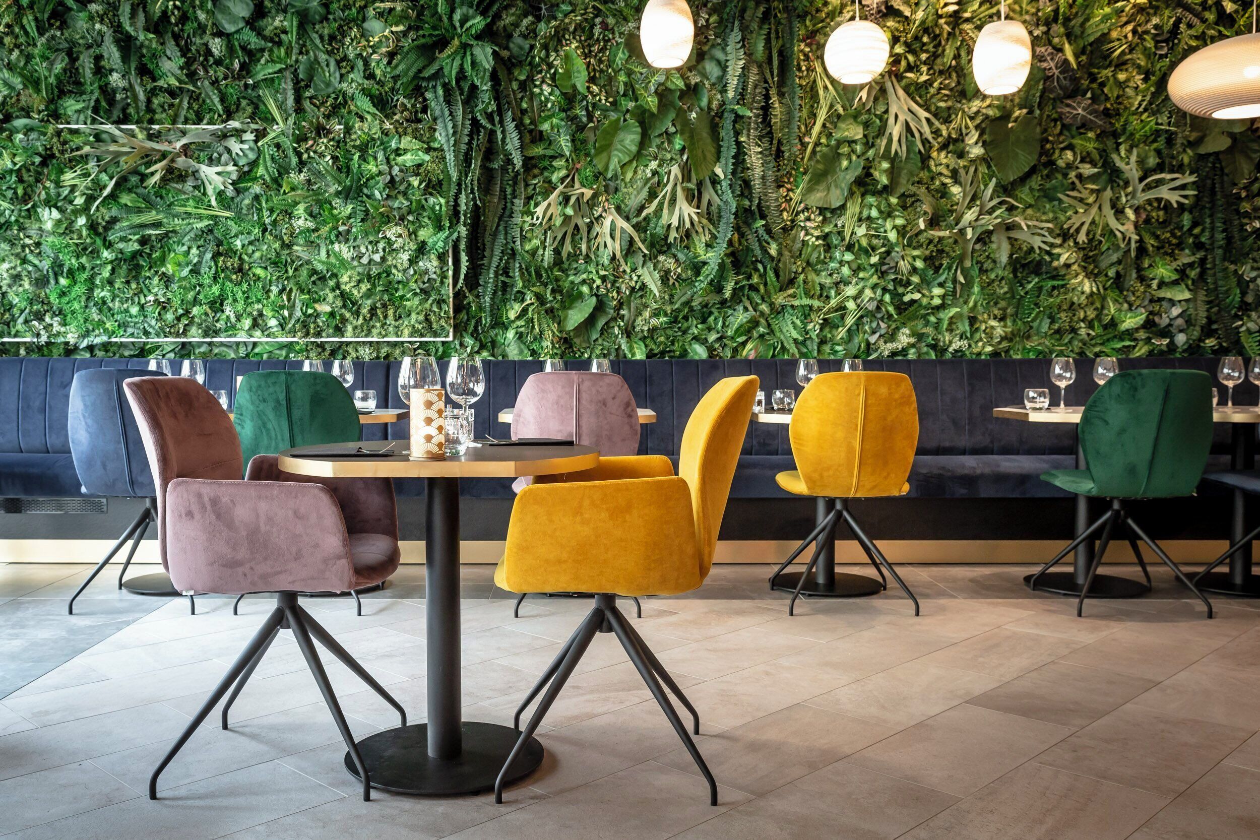 A restaurant interior with a green wall, round tables, and chairs with black legs.