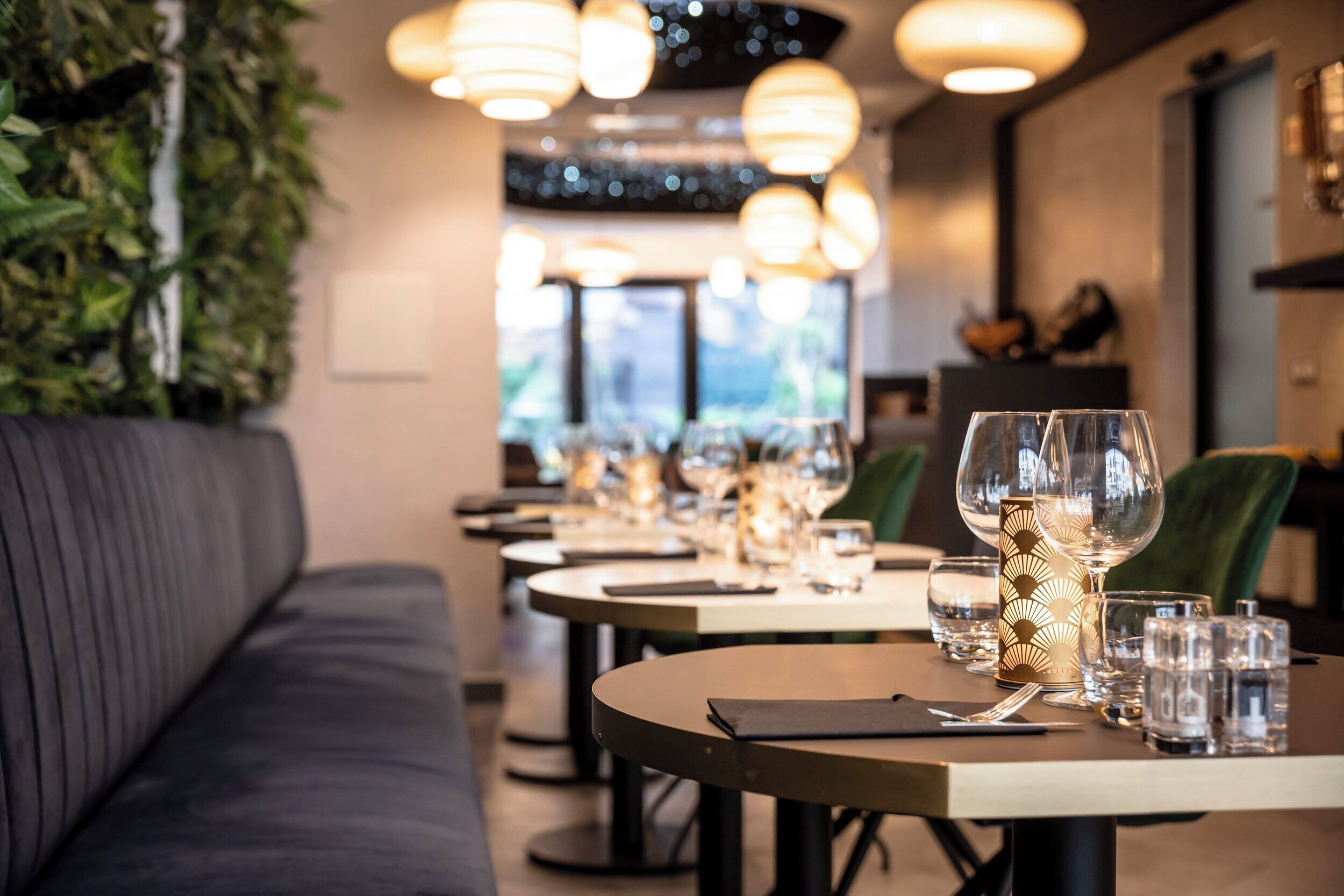 A restaurant interior with round tables, some with wine glasses and water glasses, and a sofa in the foreground.