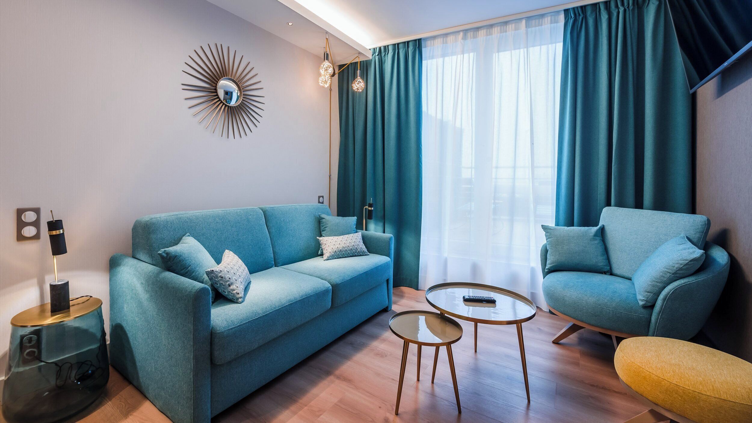 A modern living room with a sofa, armchair, and coffee table, featuring a sunburst mirror and pendant lighting.