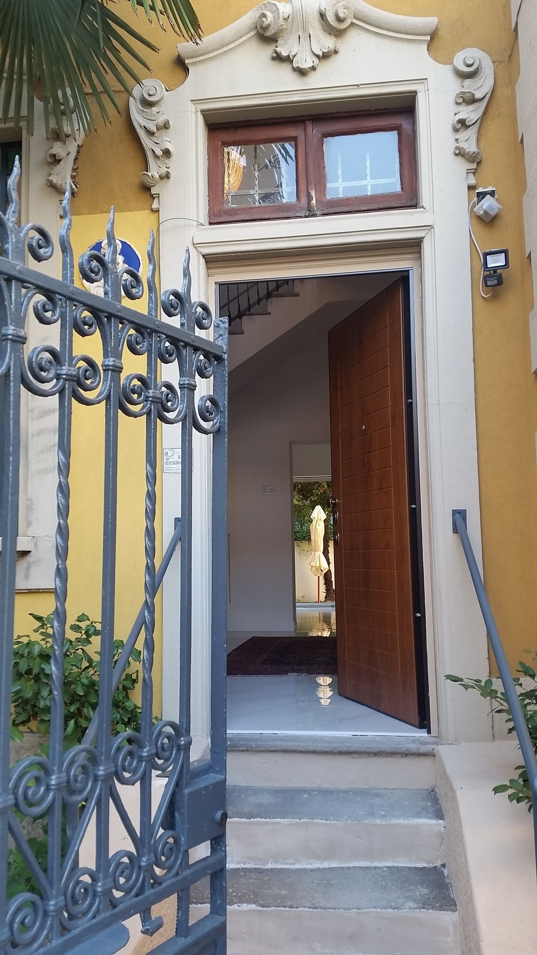 Une entrée d’immeuble avec un portail en fer forgé, une porte en bois et une petite fenêtre située au-dessus de la porte.