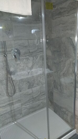 Zona de ducha con paredes de azulejo de mármol y cabina de cristal.