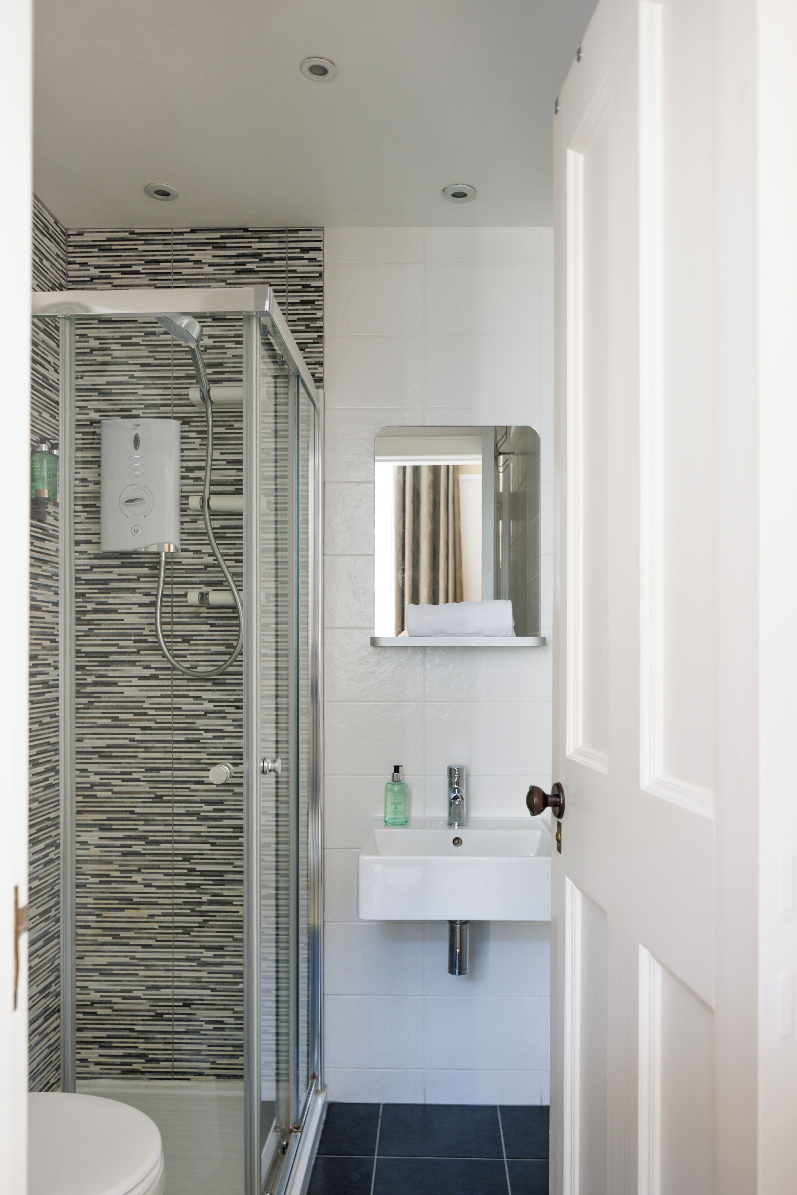Un baño moderno con ducha compartimentada por vidrio, un lavamanos blanco y un espejo encima.