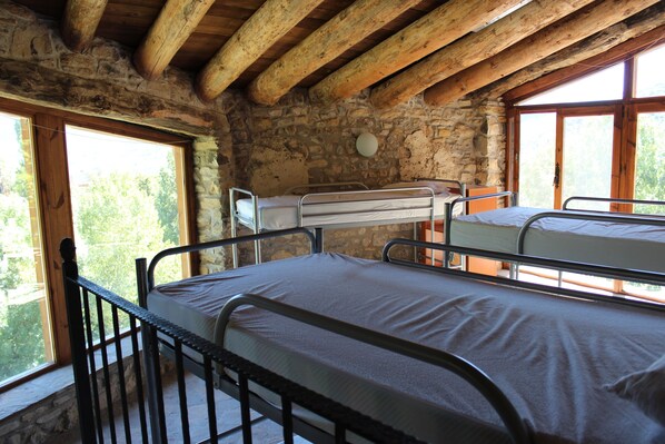A rustic cabin with two metal bunk beds, stone walls, and large windows offering a view of greenery.