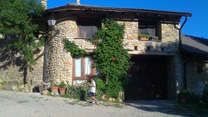 A stone house with a stone chimney, a window with a curtain, and a person standing in front. - Albergue Casa Fumenal (Valle de Lierp)