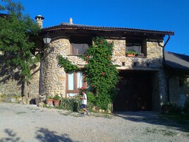 Una casa de piedra con chimenea de piedra, una ventana con cortina, y una persona de pie al frente.