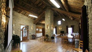 A rustic interior with stone walls, wooden beams, and a dining area with chairs and tables. - Albergue Casa Fumenal (Valle de Lierp)